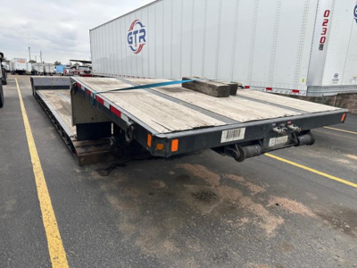 Flatbed trailer in a used trailer lot showing a Fontaine Renegade double drop expandable trailer with wooden deck, spare block, and rear lighting.
