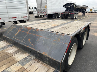 Trailer deck with dual rear axles and a steel gravel shield showing wear, Fontaine Renegade trailer with wood deck in a truck yard.