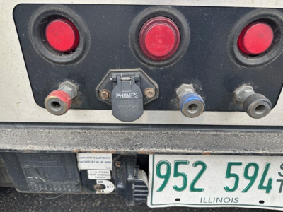 Trailer rear showing hydraulic connections and electrical sockets with red circular lights; includes 5th wheel or hitch area and Illinois license plate 952 5949.