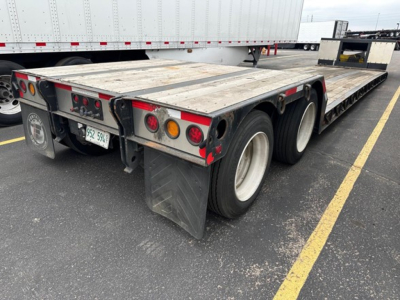 Trailer rear view showing triple-axle flatbed with wooden deck, taillights, mud flaps, and license plate. Fontaine Renegade trailer details visible.