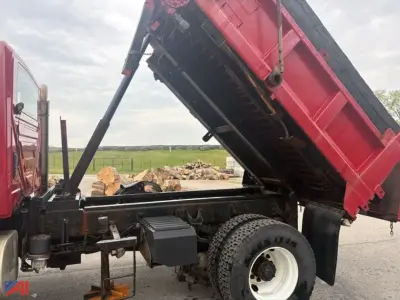 Truck chassis with dump bed raised showing hydraulic cylinder and frame; plow, wing, and sander equipment present.