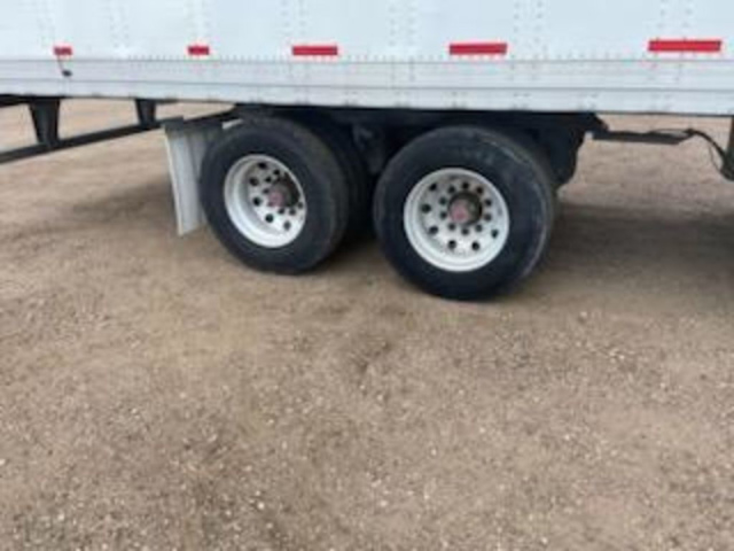 Wheel end of a Stoughton van trailer showing dual rear axles with white rims and tires, mud flaps, and a portion of the sidewall.