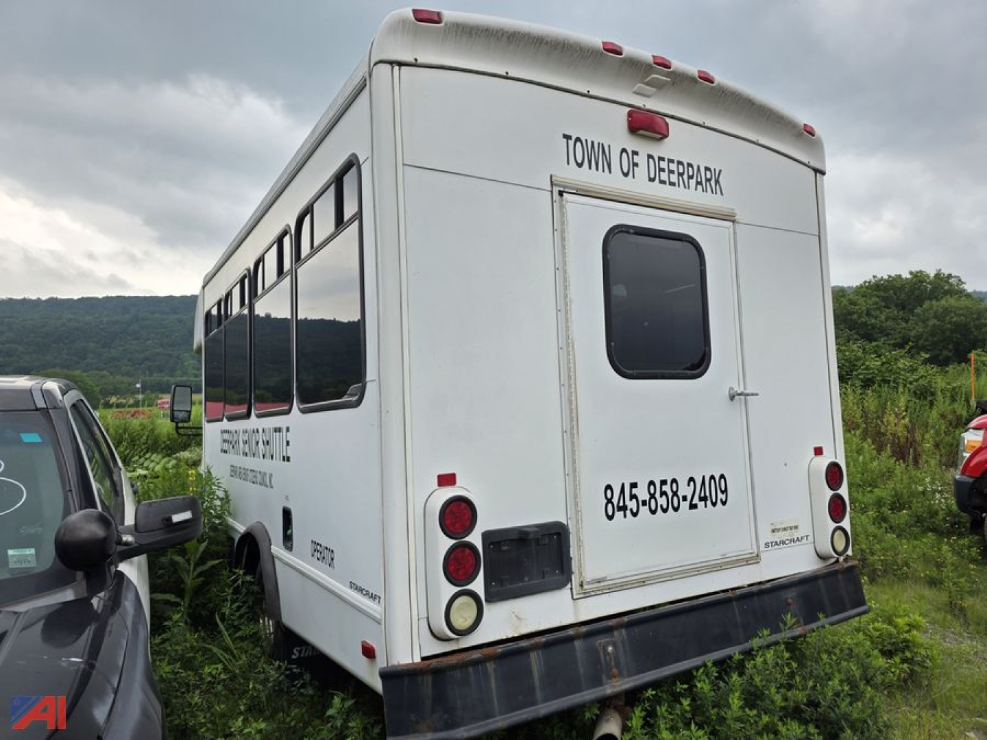 Rear view of a white Ford E-350 wheelchair bus with Town of Deerpark lettering, bus windows, and rear bumper with red tail lights.