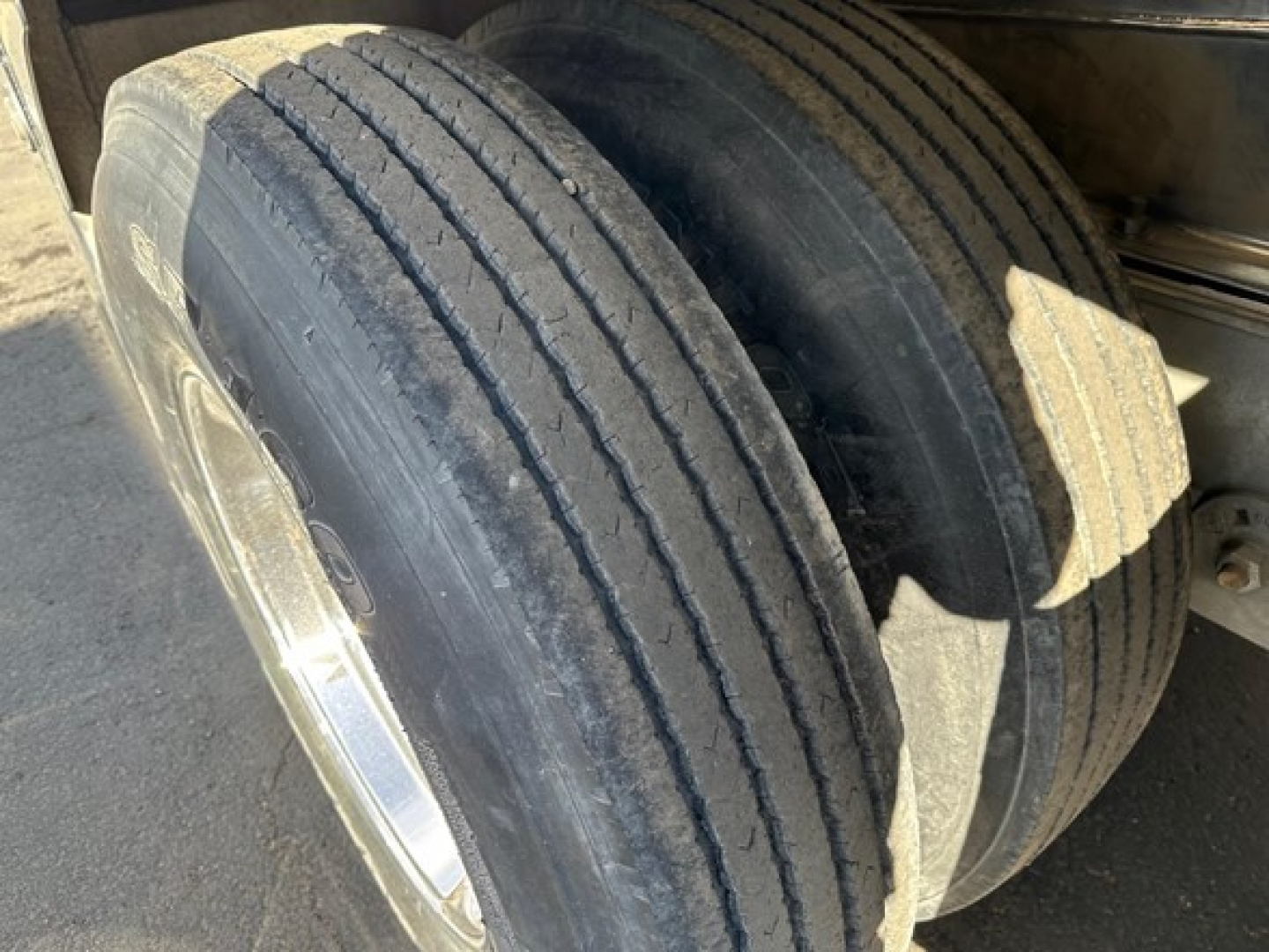 Trailer axle with dual tires and polished aluminum wheel showing tread and undercarriage detail.