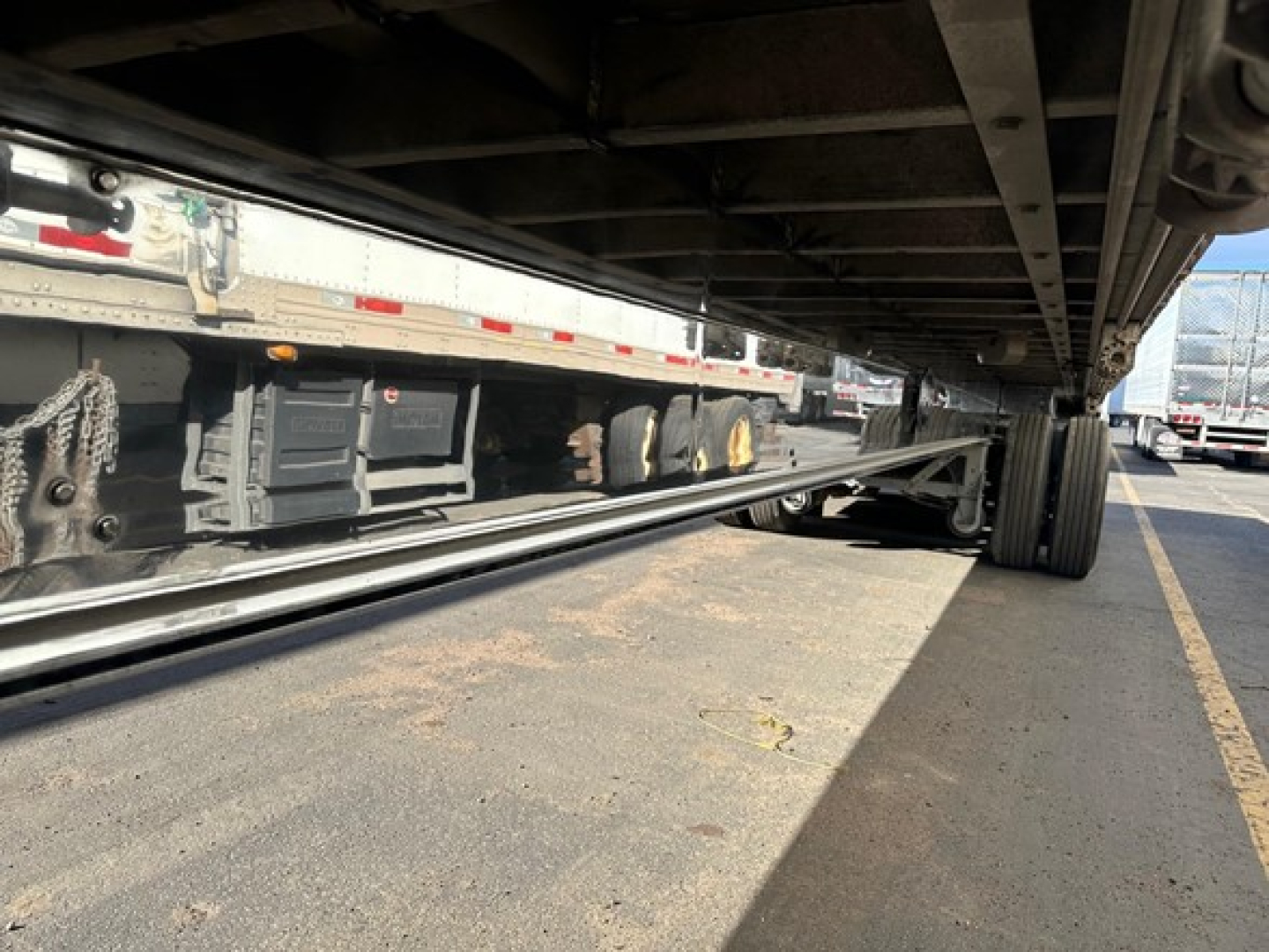 Flatbed trailer undercarriage with polished aluminum coating and dual rear wheels.