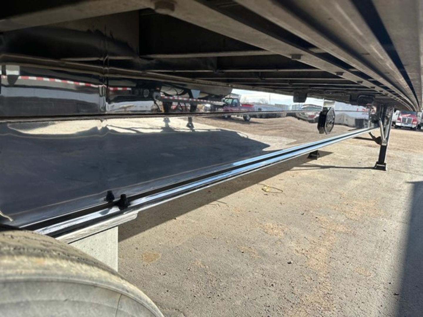 Flatbed trailer underside with polished aluminum deck and chrome side rail, support jacks visible, long reflective surface.