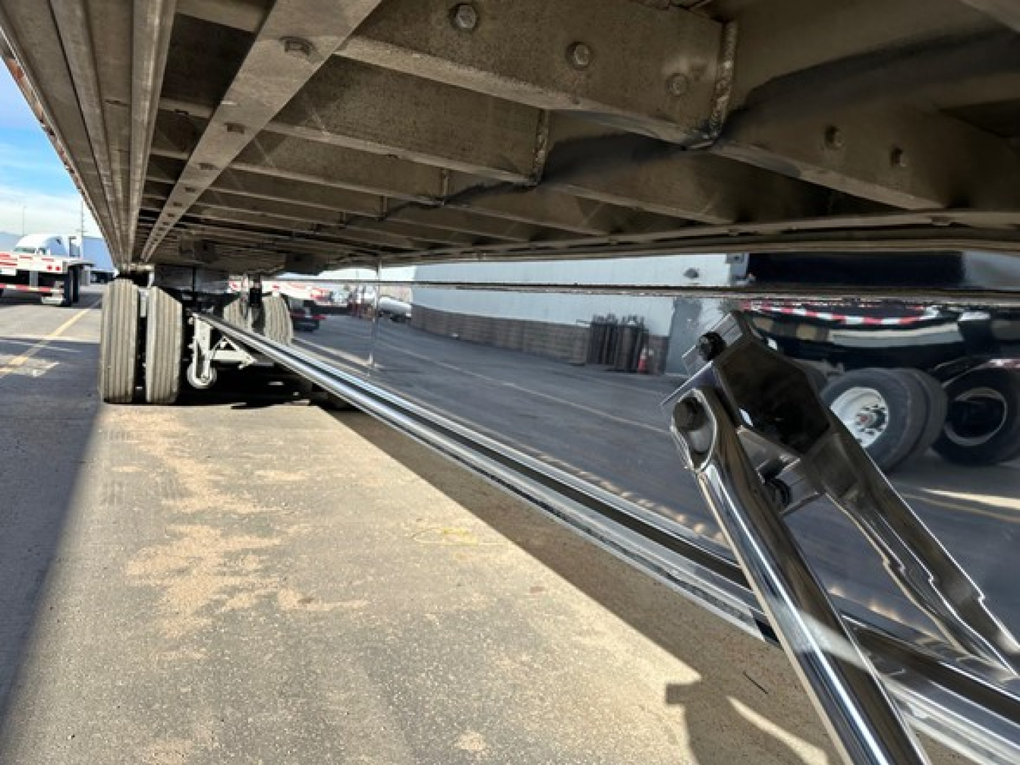 Flatbed trailer underside with polished all-aluminum framing and support beams, hydraulic lift mechanism, and longitudinal rails visible.