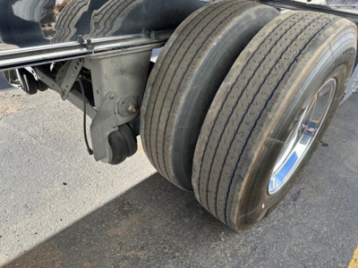 Dual rear tires of a Mac flatbed trailer showing polished aluminum wheels and suspension components.