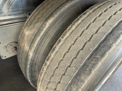 Two large trailer tires on a Mac polished all aluminum flatbed trailer showing tread pattern and sidewall markings.