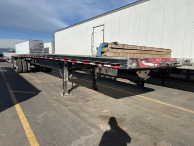 Flatbed trailer with polished aluminum deck and undercarriage, extended length, side rails, and landing gear visible.