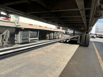 Flatbed trailer undercarriage with polished aluminum coating and dual rear wheels.