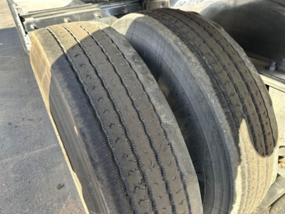 Twin axle trailer tires and polished aluminum flatbed frame showing wear on tread and sidewall.