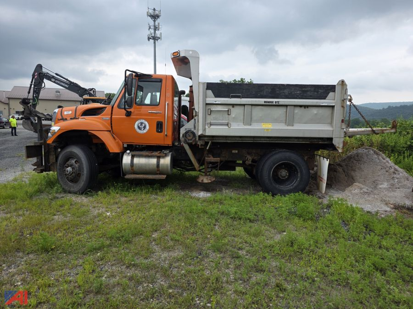 International WorkStar 7500 dump truck side view showing orange cab and white dump bed with hydraulic lift, on-site dirt pile.