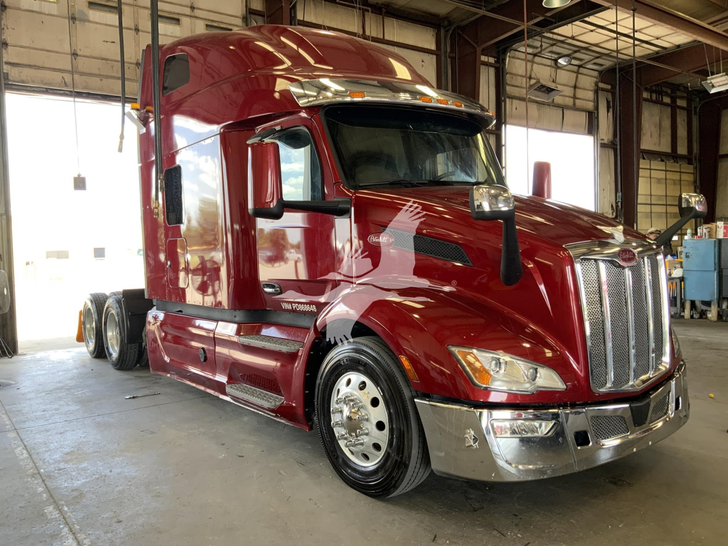 Used 2023 Peterbilt 579 conventional sleeper truck in a showroom, maroon paint, front chrome grille, large side mirrors, 6x4 tractor with dual rear axles.