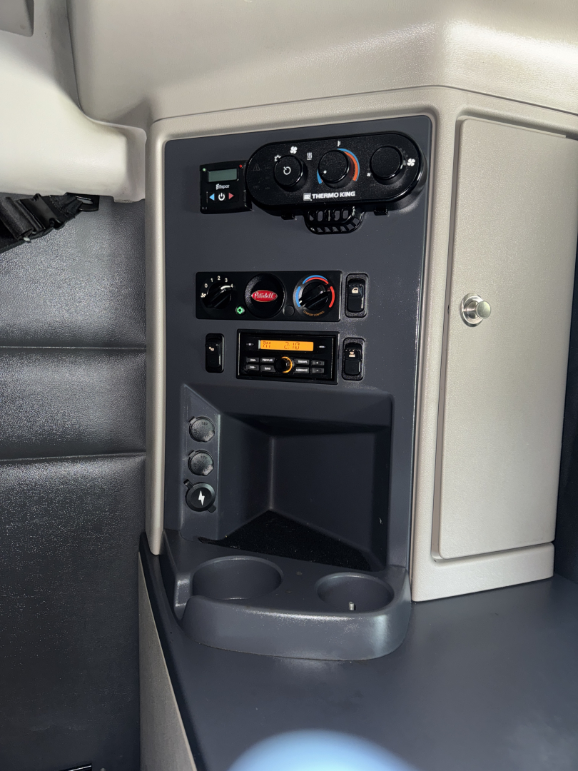 Interior console of a Peterbilt truck showing climate controls, radio/CD player, and cup holders. Visible text includes 'THERM' on a control, and various knob labels; dashboard panel with vents and storage cubby.
