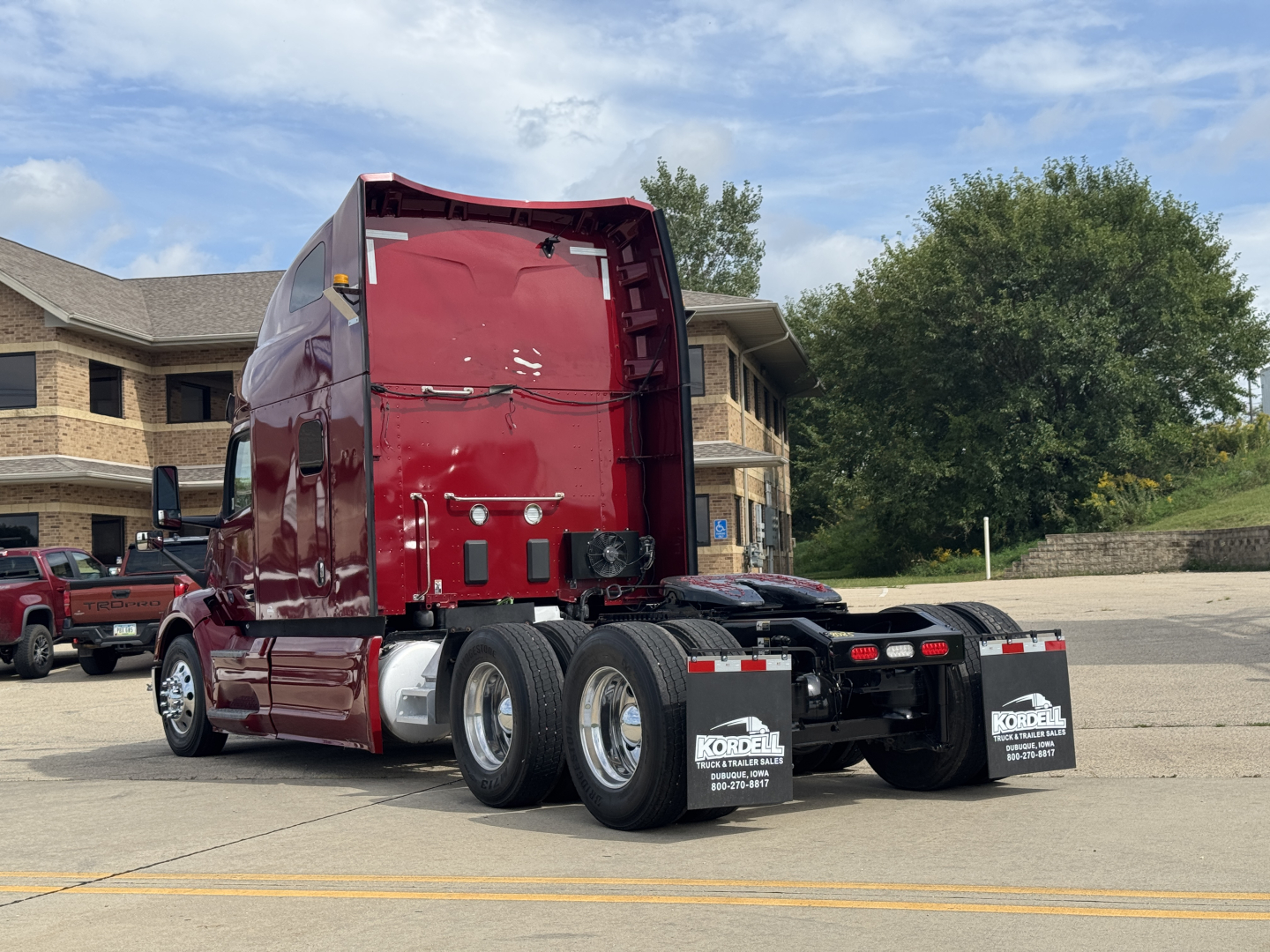Peterbilt 579 tractor in red with sleeper cab, rear view showing dual rear axles and fifth wheel, stock number 2608085_APU, from a dealership lot.