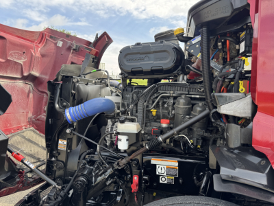 Peterbilt 579 engine bay with visible air intake, coolant reservoir, hoses, and wiring; front left fender open showing engine components and battery area.
