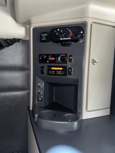 Interior console of a Peterbilt truck showing climate controls, radio/CD player, and cup holders. Visible text includes 'THERM' on a control, and various knob labels; dashboard panel with vents and storage cubby.
