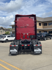 Rear view of a red Peterbilt truck sleeper cab with detached hood raised, showing dual rear mudflaps with Kordell Truck Center branding, parking lot.