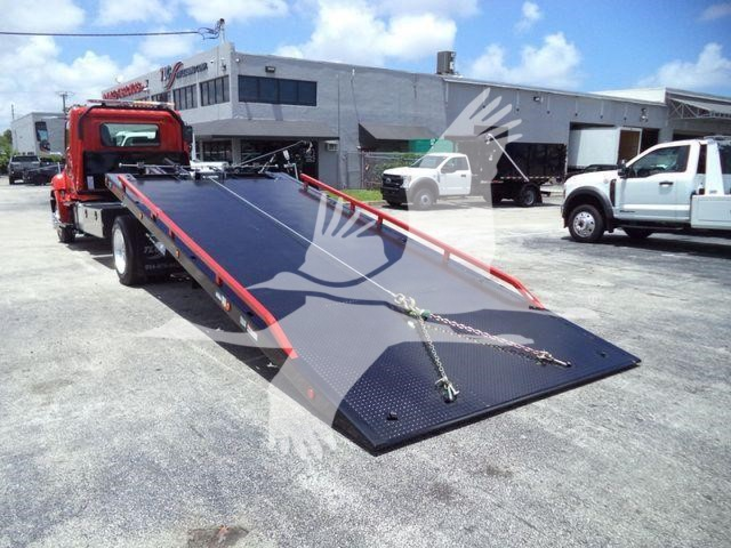 Hino 268A rollback tow truck with lowered flatbed and industrial surroundings.