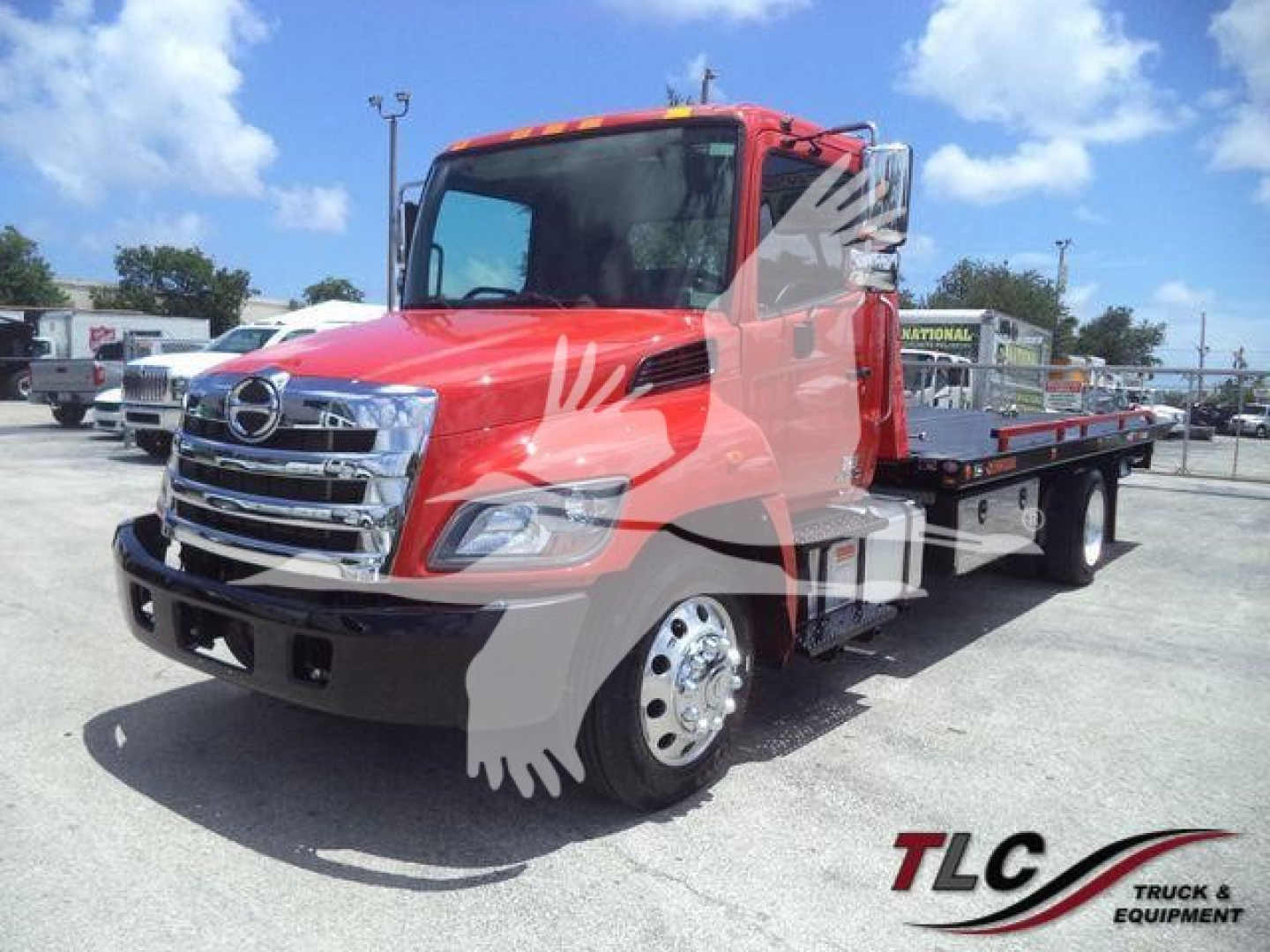 Hino 268A rollback tow truck in red with chrome front grille and flatbed, side view showing dual rear axles and wheel covers, dealership lot background.