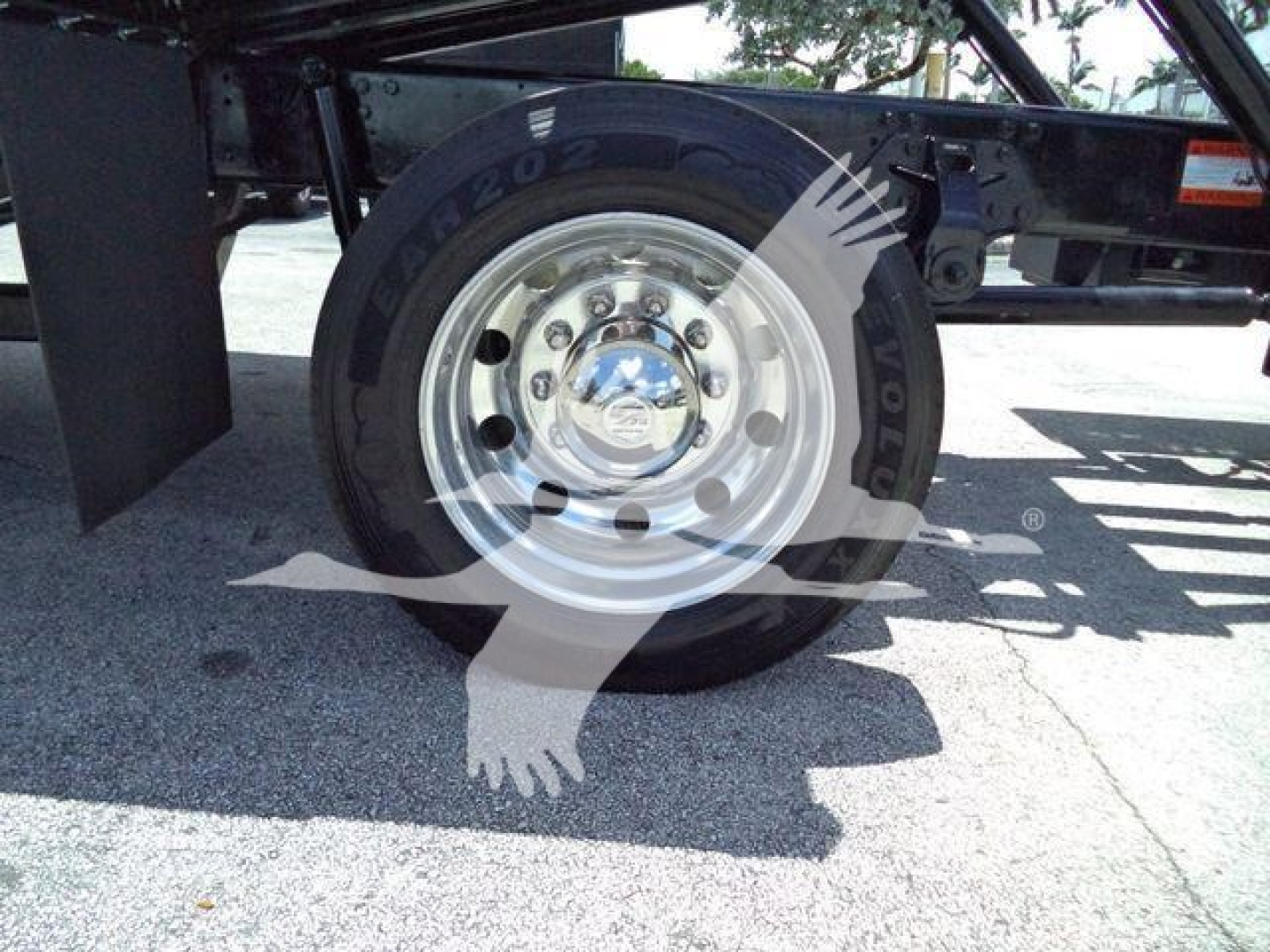 Wheel and tire assembly on truck with chrome hubcap and Rim Plus tire label visible; partial frame and undercarriage in background.