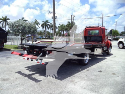 Flatbed tow truck in a lot. Visible text includes stock number T75219FM and vehicle type categories in the listing background.