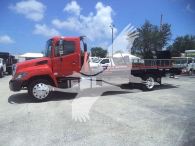 Red 2020 Hino 268A rollback tow truck in a lot with other vehicles; side view shows flatbed and dual rear wheels; no visible manufacturer text on cab.