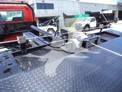 A 2020 Hino 268A rollback truck with a metal diamond plate bed and hydraulic winch, seen from the back of the truck with other equipment in the background.