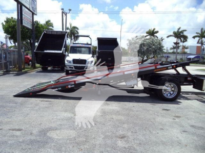 Hino 268A rollback tow truck with flatbed in lowered position, two white cab trucks in background, palm trees, dealership lot.