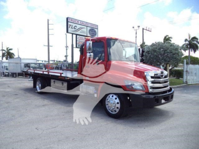 2000s- era Hino 268A rollback tow truck with red cab and flatbed, side view showing chrome grille, large side mirrors, and dual rear wheels.