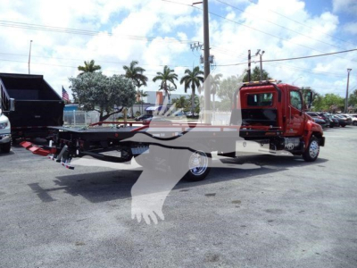Hino 268A rollback tow truck with a red cab and extended flatbed, side view showing crane and ramps.