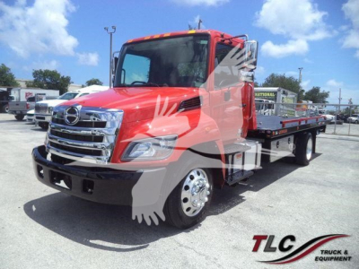 Hino 268A rollback tow truck in red with chrome front grille and flatbed, side view showing dual rear axles and wheel covers, dealership lot background.