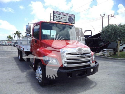 Front-left view of a red 2020 Hino 268A rollback truck with chrome grille, side platform, and dual rear wheels in a dealership lot.