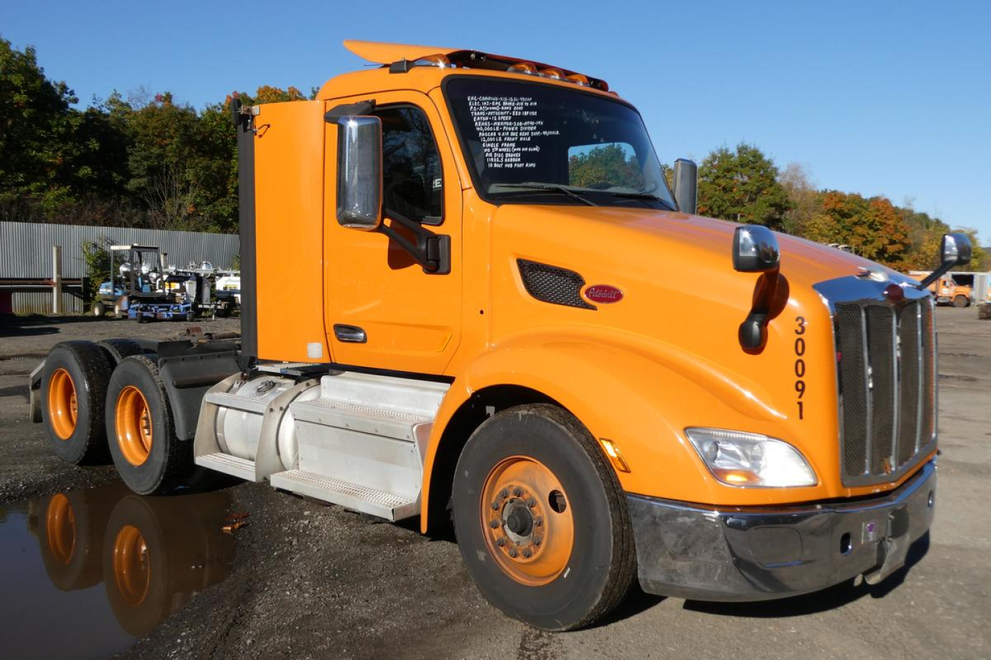 Peterbilt 579 daycab truck in orange, side view showing cab and front grille with White text on windshield label and blue sky.