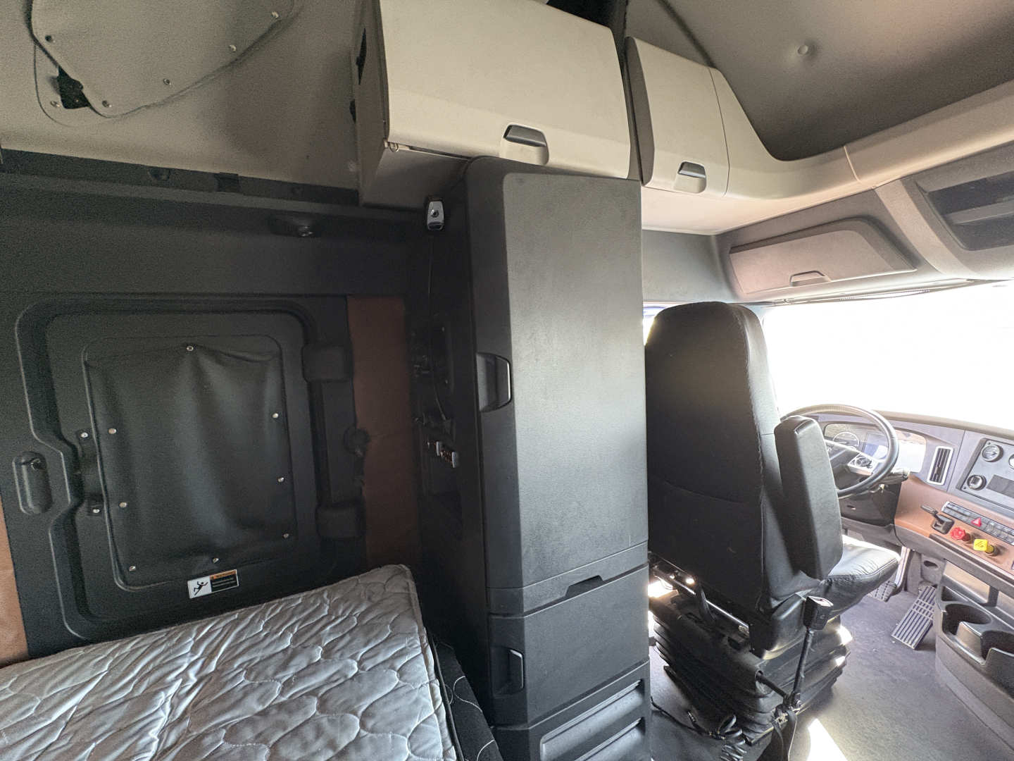 Cab interior of freightliner cascadia 126 showing captain seat and overhead cabinets with a tall central cabinet unit.