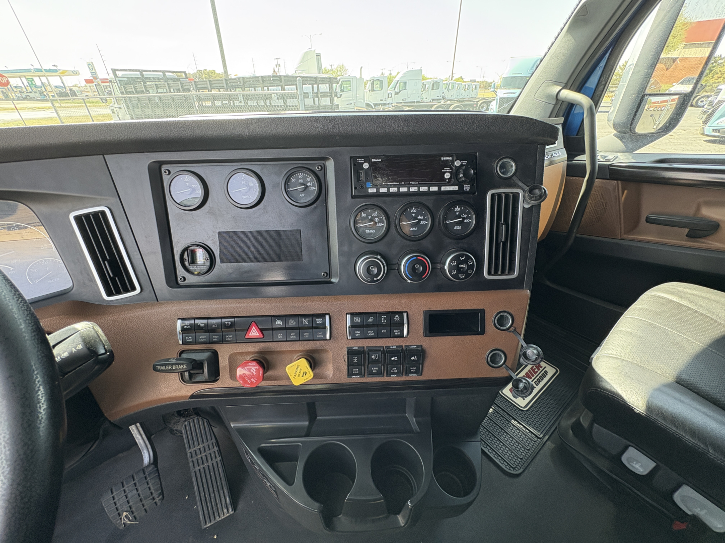 Dashboard controls of a 2022 Freightliner Cascadia 126 truck interior with gauges, switches, and cup holders visible.