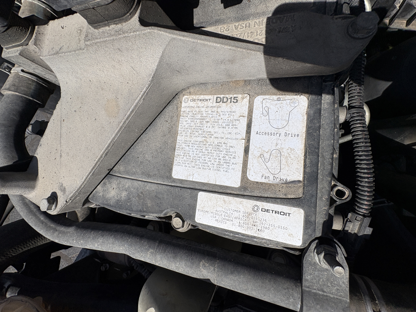 Detroit DD15 engine control module label visible under hood with warning stickers and wiring harnesses.