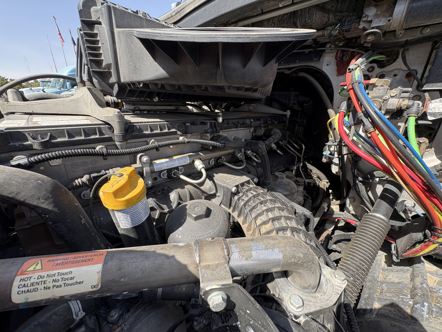 Freightliner Cascadia 126 engine bay showing large intake ducting, yellow oil cap, and colorful engine wiring harness, view of front left side