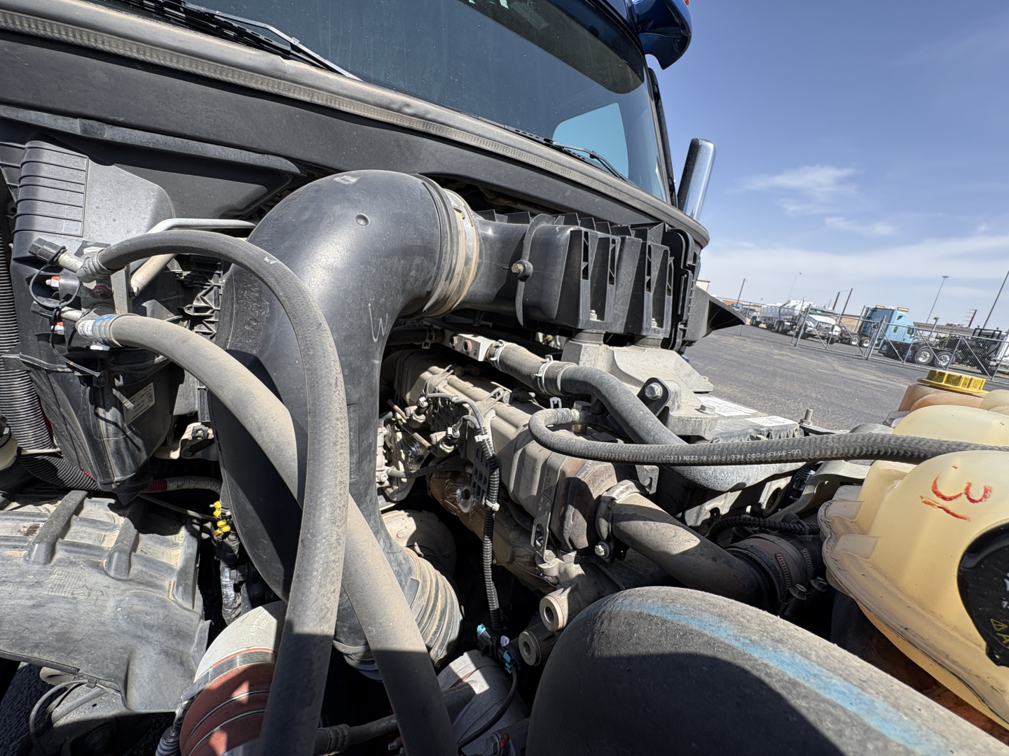 Truck engine bay of a 2022 Freightliner Cascadia 126 showing hoses, coolant reservoir, and engine components.