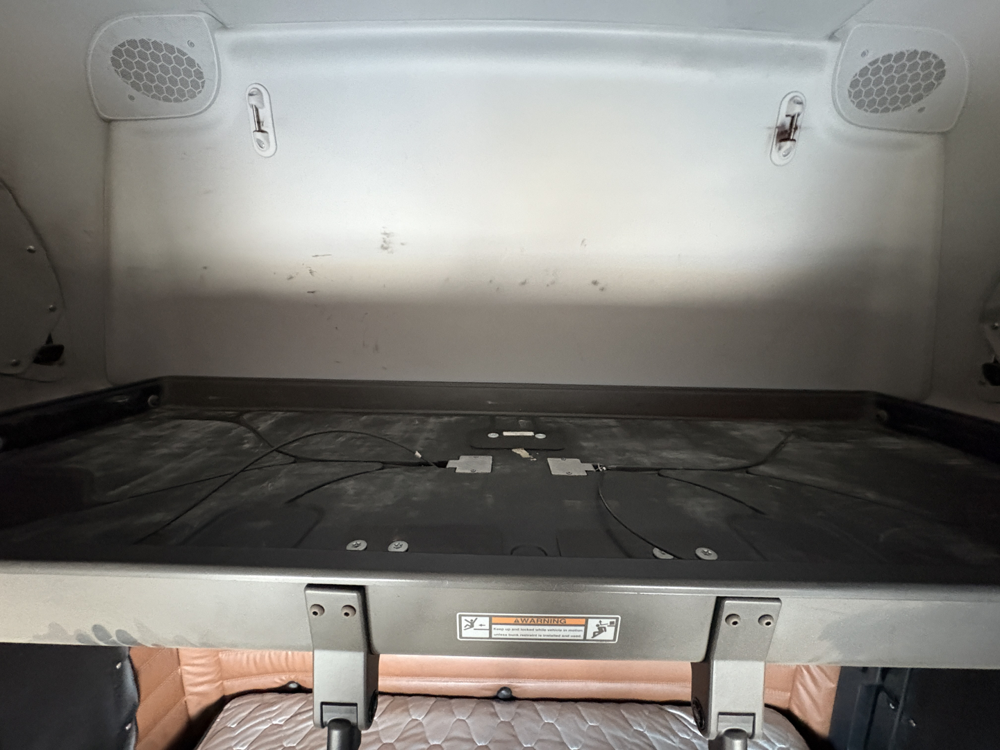 Freightliner Cascadia 126 sleeper cab interior cargo area showing plastic side panels and storage shelf with cables in bed area.