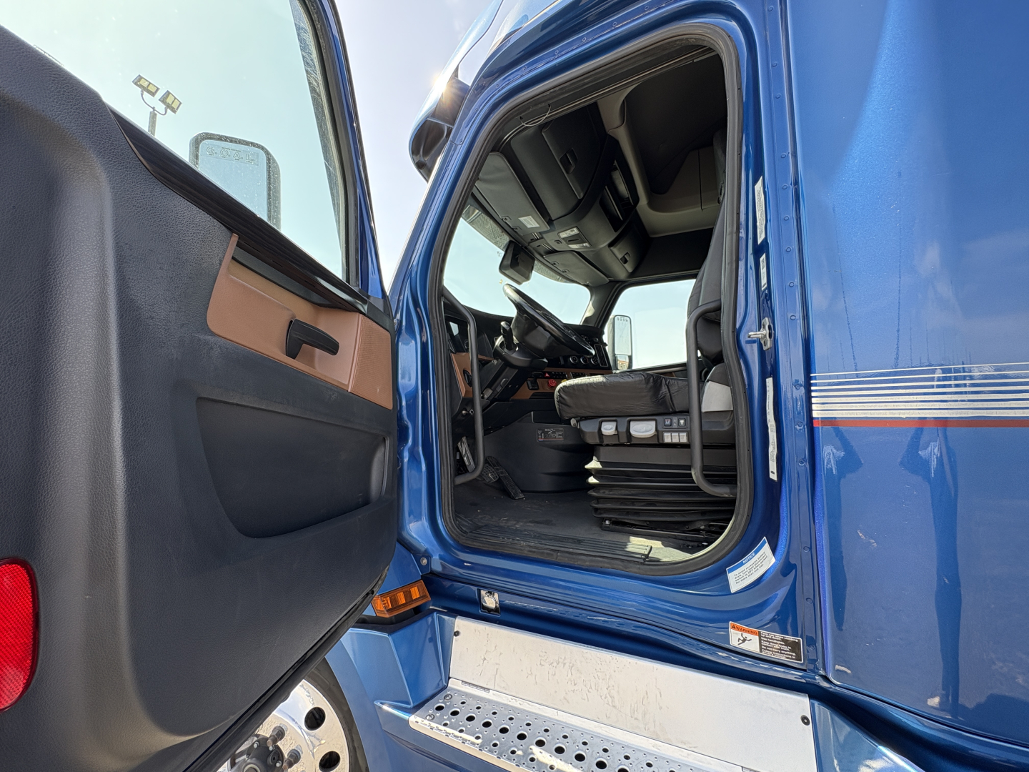 Truck cab interior visible through open door of a blue 2022 Freightliner Cascadia 126. Steering wheel, driver's seat, and dashboard visible; door panel with handle; truck sill and side of step visible.