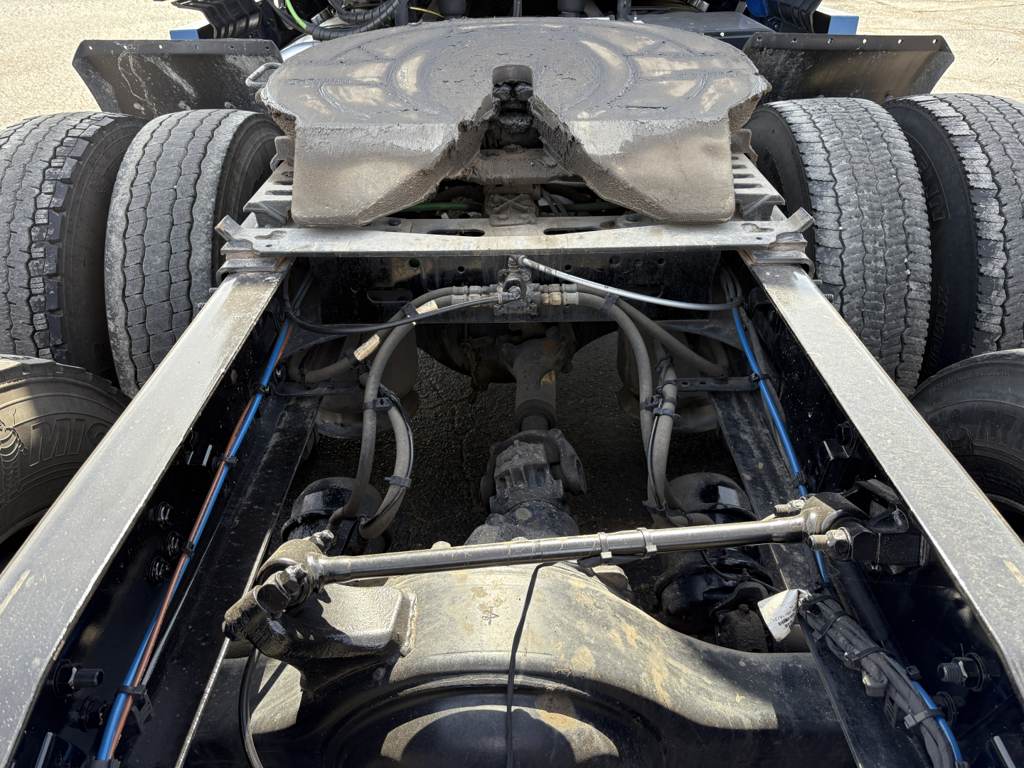 Front view of a Freightliner Cascadia 126 truck rear chassis showing drivetrain and suspension components, dual rear wheels, fuel lines, and universal joints.