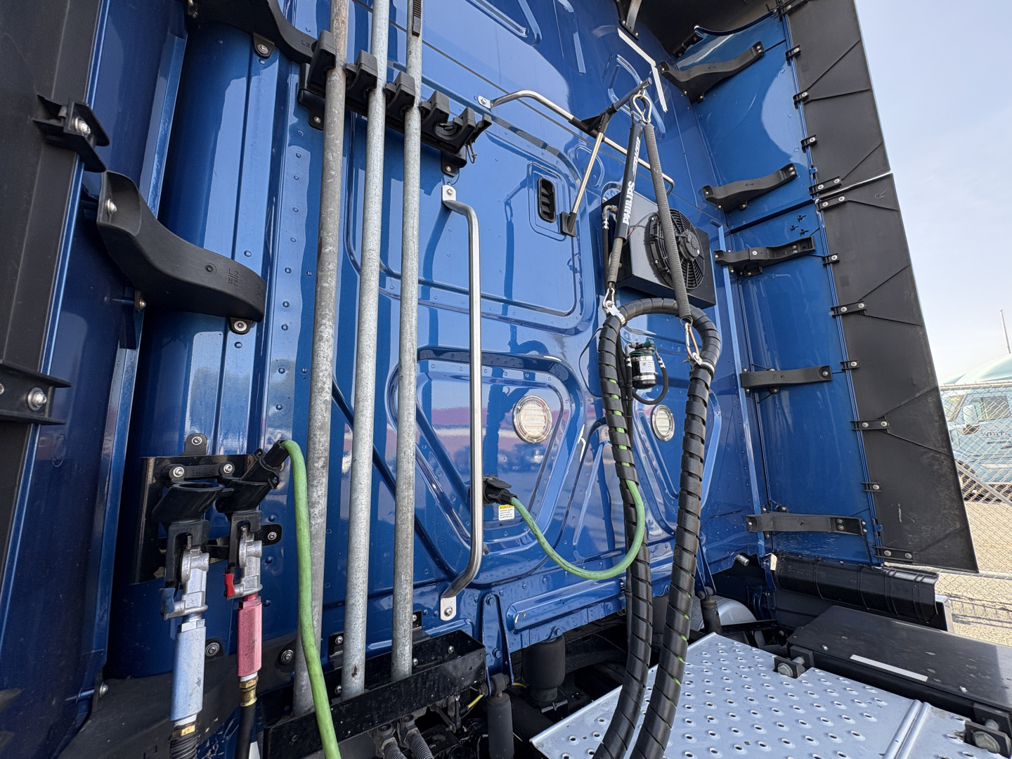 Truck cab interior rear view showing vertical bars, hoses, and wiring harnesses inside blue Freightliner Cascadia 126 sleeper compartment.