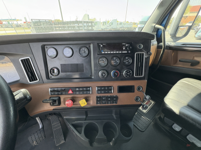 Dashboard controls of a 2022 Freightliner Cascadia 126 truck interior with gauges, switches, and cup holders visible.