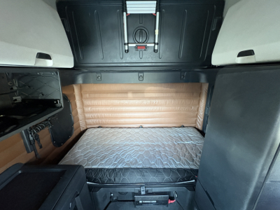 Freightliner Cascadia 126 sleeper cab interior featuring bunk bed with quilted mattress, side panels, and storage compartments visible from rear view.