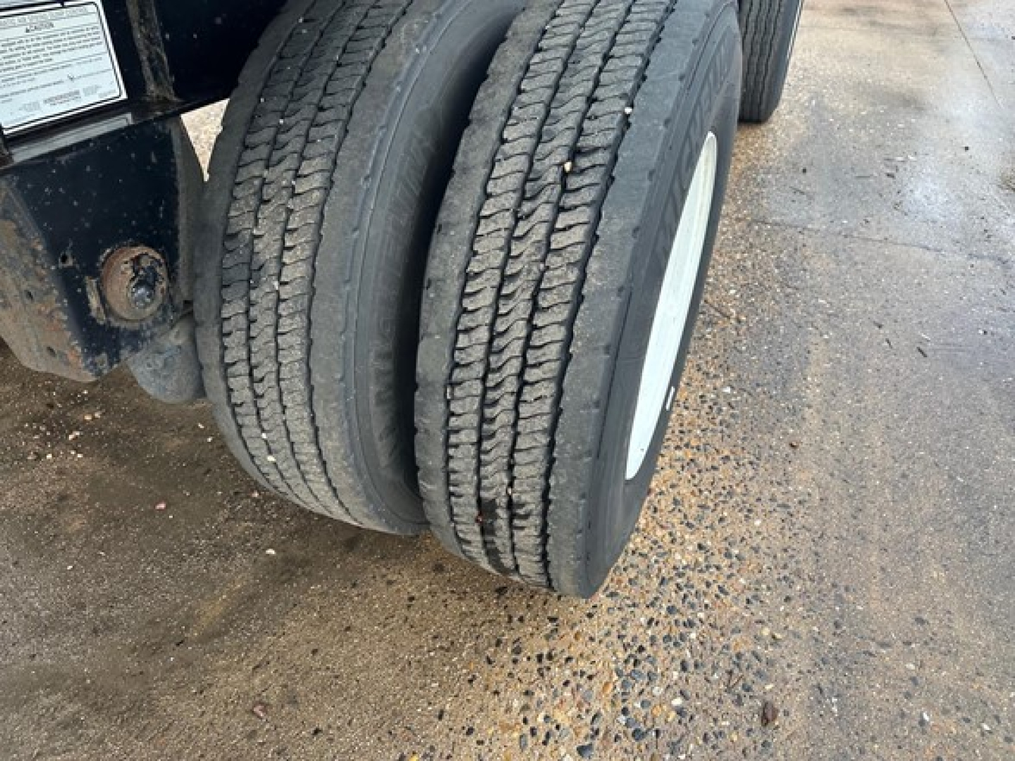Dual rear tires on Transcraft trailer with white wheel rims and muddy ground surface.