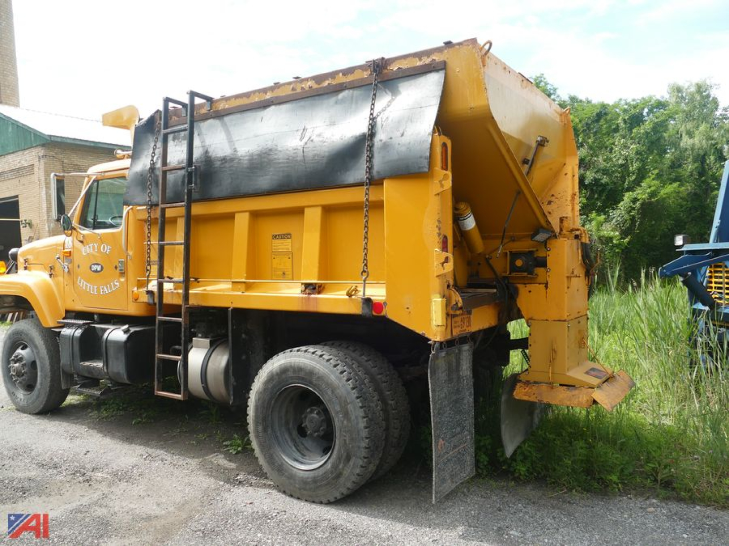 Dump truck with sander attachment showing side view and rear hopper, yellow paint, black reservoir cover, ladder, and large tires