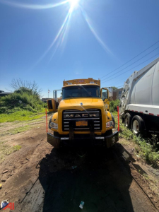 Front view of a yellow 2014 Mack garbage truck with black grille guard and burned brand name, visible cab and dump body; license plate is centered on bumper.
