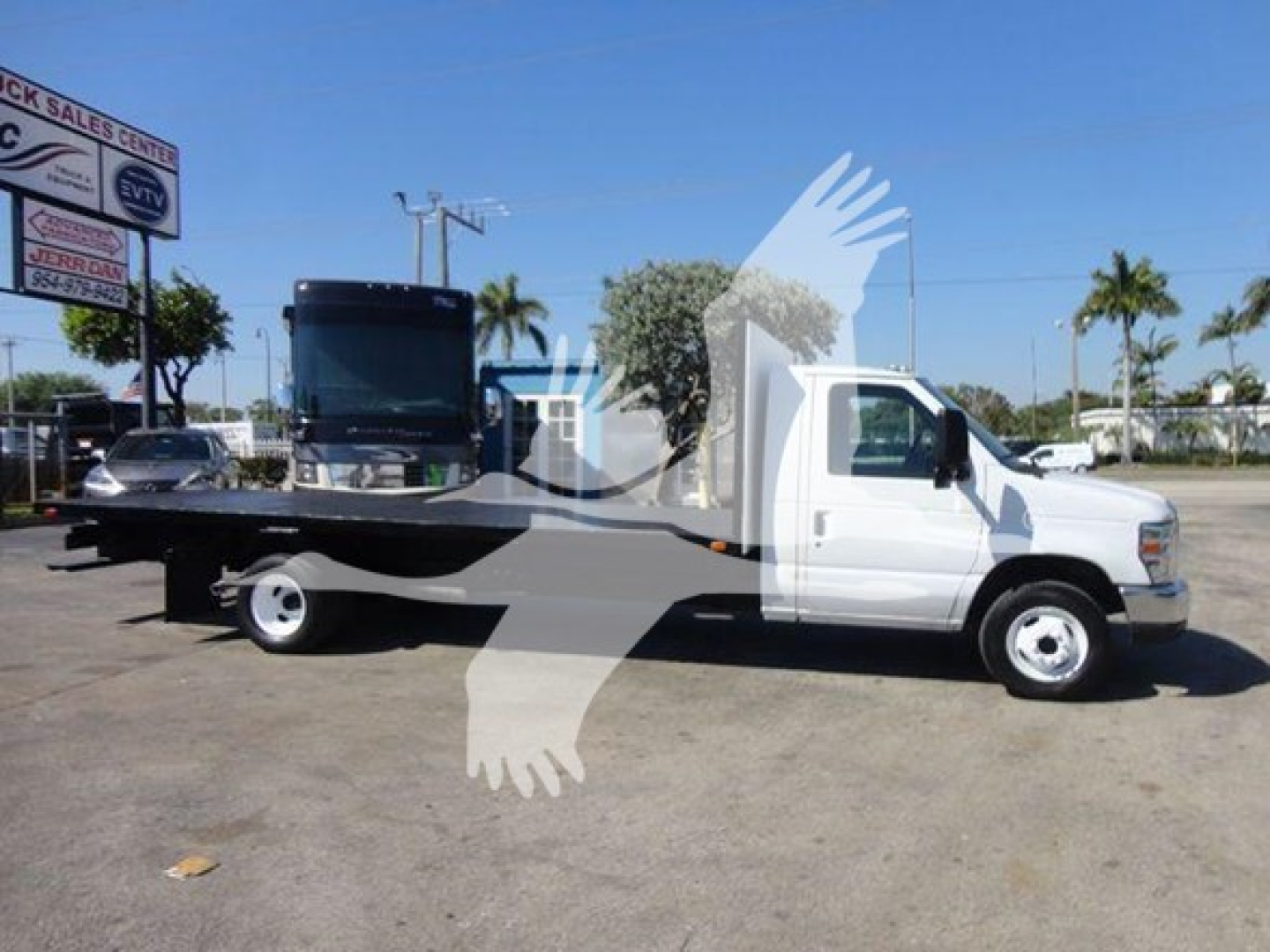 Flatbed tow truck side view showing white cab and black flatbed with a tilted loading platform on 2011 Ford E450.